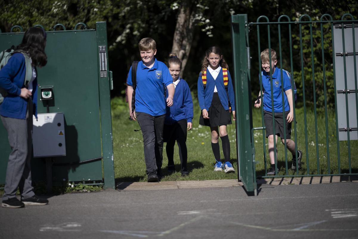 Pupils in blue uniform arriving through the school gate in the morning