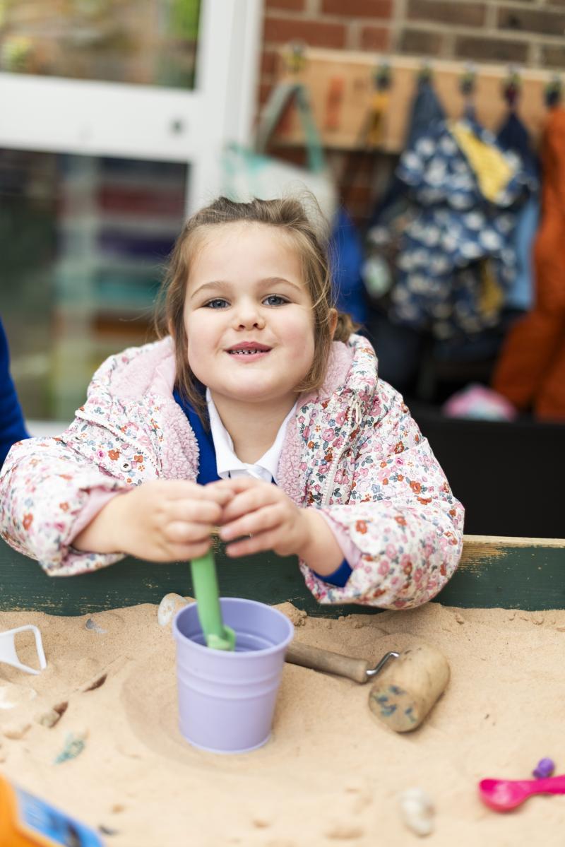 A smiling pupil playing at the sand tray in the early years outdoor area